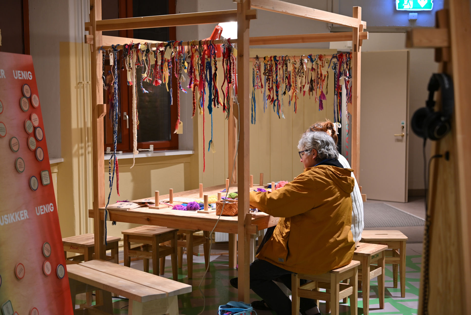 To damer sitter ved et håndverksbord og fletter