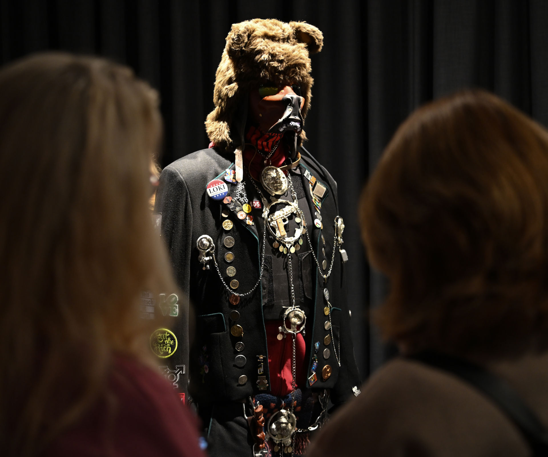 Bjørnelignende figur i en sort folkedrakt med buttons, strykemerker, søljer og annet montert på.