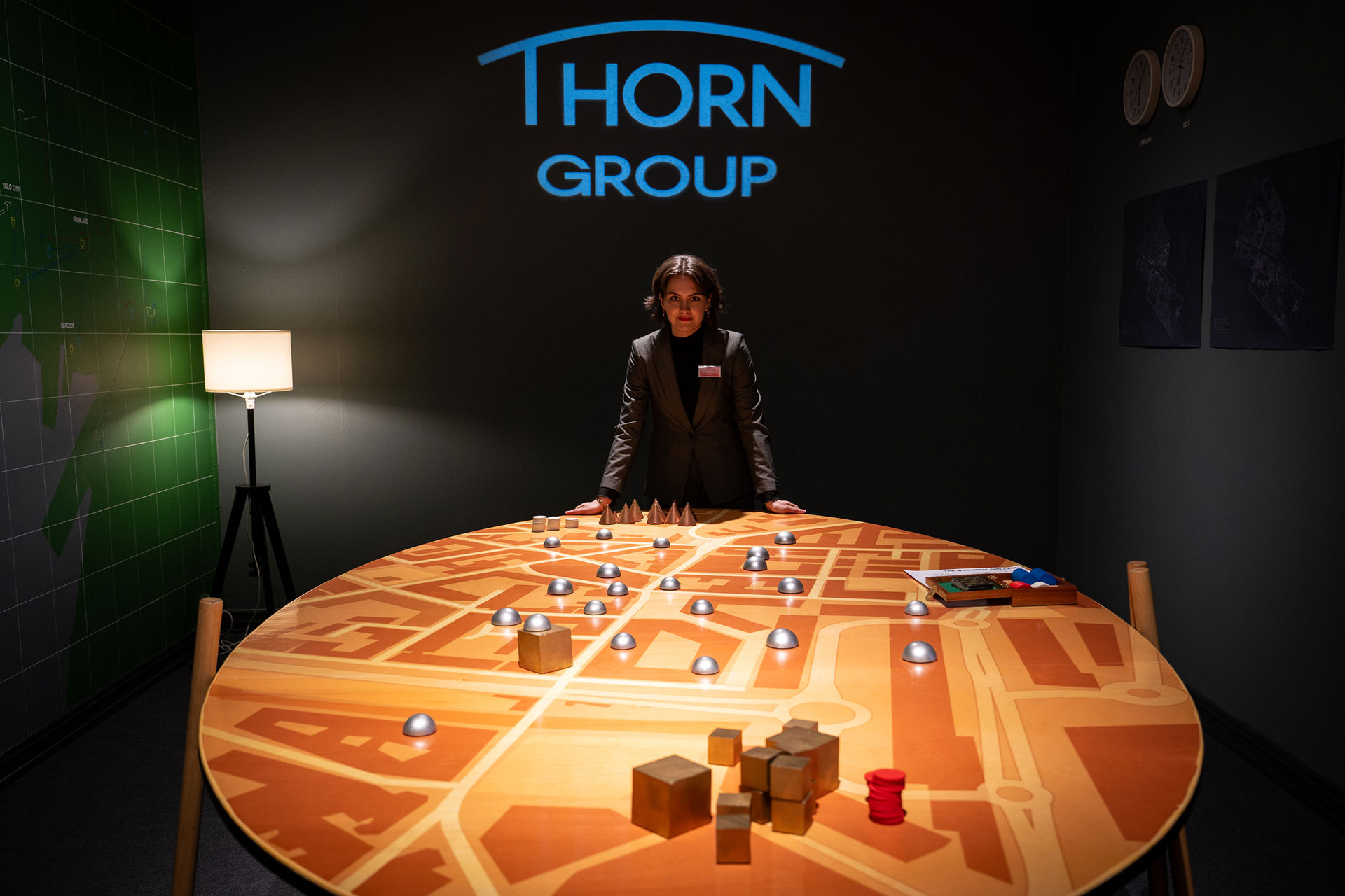 Dame i dress i et mørkt rom lener seg på et stort spillbord mens hun er i kamera. Thorn Group står i store blå bokstaver på veggen bak.