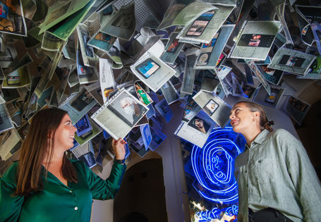 To unge kvinner ser på plastmapper med bilder og ulike utsagn som henger i taket.