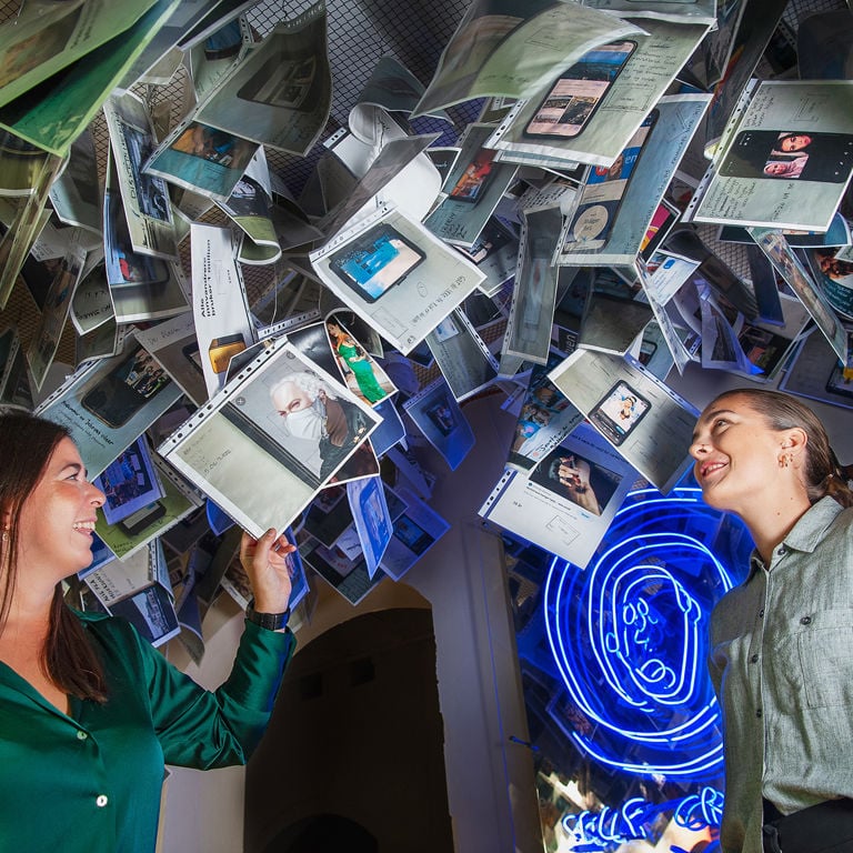 To unge kvinner ser på plastmapper med bilder og ulike utsagn som henger i taket.