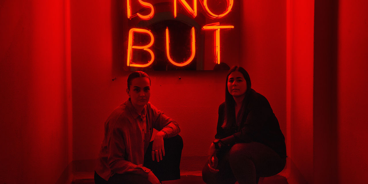 2 jenter foran neonskilt med teksten There is no but