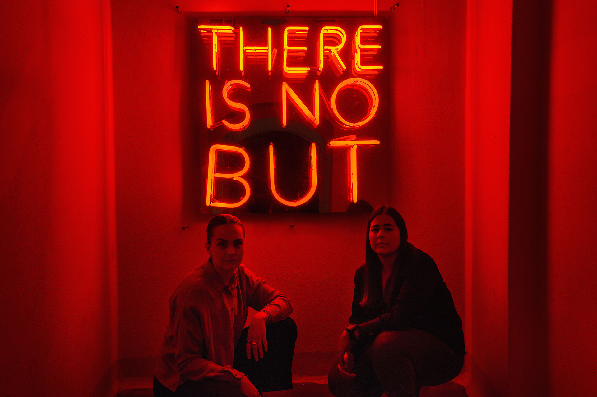 2 jenter foran neonskilt med teksten There is no but