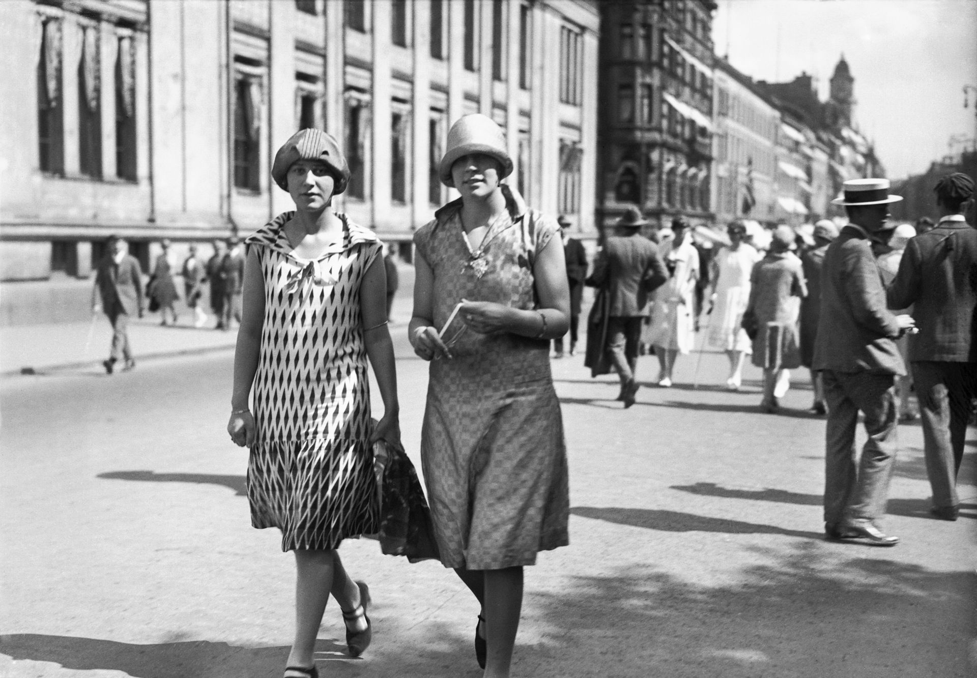 To damer kledd i 20-tallskjoler og hatter spaserer bortover Karl Johan